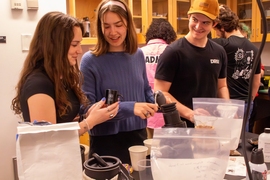 A student holds an espresso cup at a lab table while talking to her two classmates.