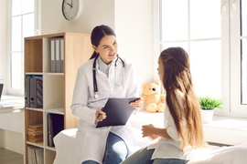 A doctor speaks with her patient, a young girl, while holding a chart