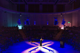 A woman performs violin in a circular music hall, with blue lighting and a white spotlight