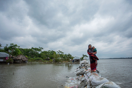 Woman and children walk over sandbag embankment in Bangladesh