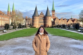 Crystal Liang, wearing a winter jacket, stands in front of a German castle with round towers and high, pointed spires