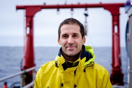 Thomas Peacock, wearing a yellow rain slicker, poses on the deck of a ship.