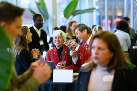 Three people laugh during a conversation in a crowded room.