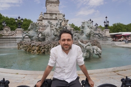 Gevorg Minasyan sits on the edge of classical sculpture fountain on a partly cloudy day.