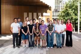 15 people pose standing together outside in front of a building.