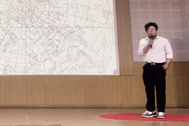 Vivan Mirchandani speaks in front of a screen, which shows graphics of constellations.