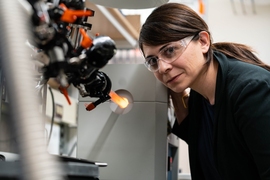 Desirée Plata in the lab wearing safety goggles and leaning over a machine.