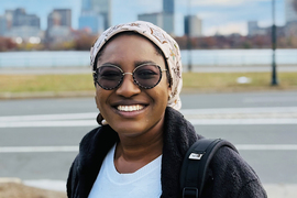 Akorfa Dagadu poses for a photo outdoors, with Boston’s skyline out of focus in the background