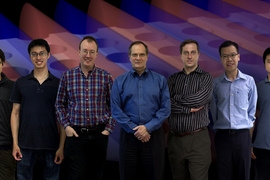 Members of the team that discovered and demonstrated the new way to trap light. From left: Bo Zhen, Chia Wei Hsu, Steven Johnson, John Joannopoulos, Marin Soljačić, Song-Liang Chua and Jeongwon Lee. The background is a snapshot of a theoretical simulation of their system, where light (its electric field shown in blue and red patterns) is confined in a slab with periodic array of holes.