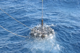 Scientists on an oceanographic research ship lower a rosette of 24 bottles into the ocean to capture samples of wild microbes in their natural habitat.