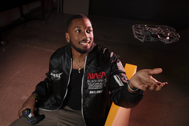 Austen Roberson smiles while looking at a small hovering drone he is piloting with a game controller.