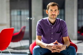 James LeBeau sits on a red chair with hands together, with blurred background