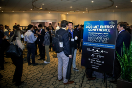 Attendees network in a large room. A blue sign says, “2023 Energy Conference. Transition under crisis: Technology, Investment, and Geopolitics. The MIT Energy & Climate Club thanks our sponsors.” There are several small logos.