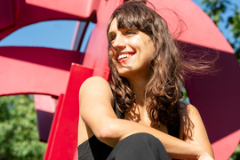 Jaye smiles while sitting down, with a red sculpture in background.
