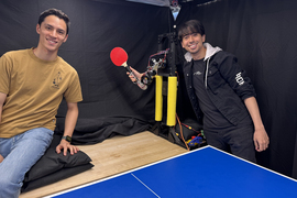 David Nguyen and Kendrick Cancio pose for portrait, as Cancio holds robotic arm with ping pong paddle.