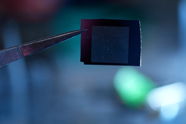 Tweezers hold a tiny black square membrane.