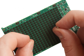 A hand holds 2 tiny beads over a green circuit board.