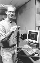 Graduate student Mark Ottensmeyer displays the latest version of PHANToM. Depending on which wall of the square represented on the computer screen one "touches" with the PHANToM, the sensation of hot, cold or a neutral temperature will be felt by the user.