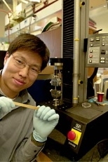 Chemical engineering research associate Yadong Wang stretches a piece of regular vulcanized rubber.  Biorubber, which is white and oaque, is stretched using the machine by his side.