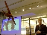 Senior research engineer Charles M. Oman reflects on the loss of his friend, astronaut Laurel Clark, at MIT's memorial observance Monday. Clark's image was shown on a screen behind a model of a monoplane hanging in the Gelb Learning Center.