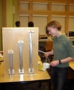 Ellen Cappo shows the column-buckling demonstration. The white bucket on the right transmits identical loads to the three wooden columns. As the bucket's load is increased, the columns buckle, starting with the longest one.
