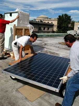 On an appropriately sunny day, Facility employees Rick Hadge, center, and John DaSilva install solar panels on the roof of Hayden Library, while Paul Lyons of Zapotec Energy uncrates the next.