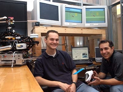 Graduate students Tom Schouwenaars, left, and Mario Valenti sit in front of an operational guidance system they  worked on which is being used  to fly an unmanned aircraft from a manned parent plane to gain surveillance in dangerous situations. They have adapted the same guidance system to the helicopter at left.