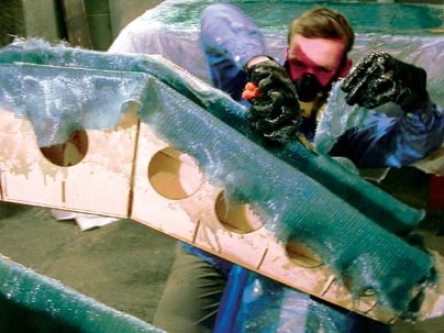 Media arts and sciences graduate student Peter Schmitt
works on the 'Muscles; mini-skyscraper mold in the MIT Paint Shop. He is cutting off excess fiberglass/epoxy cloth, the material that forms the core of the structure. The negative mold is made of plywood and cardboard.