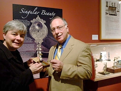 MIT Museum curator of science and technology Deborah Douglas examines a simple microscope from the exhibit, 'Singular Beauty,' with the owner of the collection, Raymond V. Giordano.