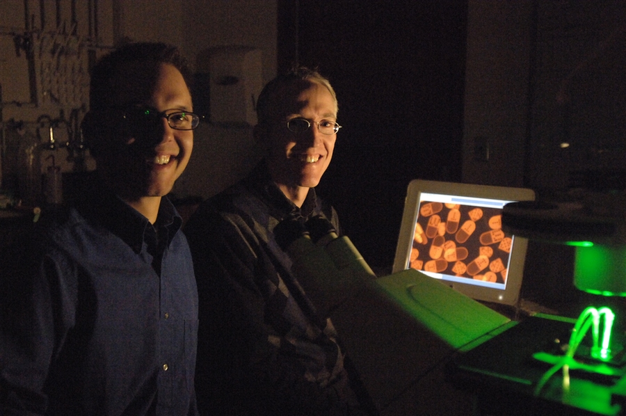 Graduate student Daniel Pregibon, left, and Associate Professor Patrick Doyle, survey microparticles on a monitor in their lab. The microparticles are on a glass slide on the microscope: Green ultraviolet light is shone on it to help view the particles. The particles are designed to detect specific DNA sequences.