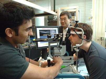 Professor James Fujimoto, center, with students using the eye-imaging technique he began developing in the early 1990s. With his head in the apparatus is Desmond C. Adler and at left, taking measurements, is Vivek Srinivasan. Adler and Sriinivasan are both graduate students in electrical engineering and computer science.