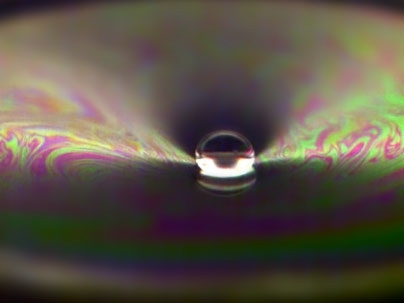 A drop of water bounces off a soap film.