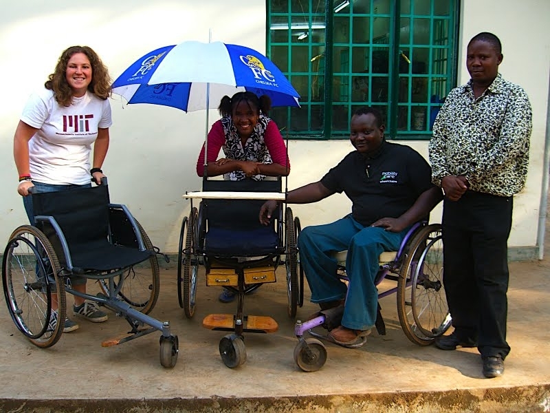 Tish poses with the folding three-wheeler and small business wheelchair prototypes. From left, Tish, Agnes Michael, Daniel Namkessa, and Lucas Tanaki 