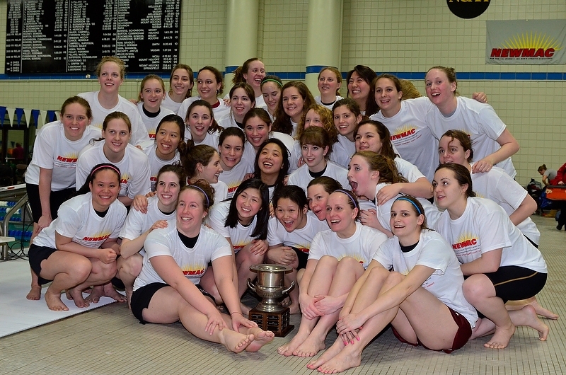 The MIT Women's Swimming and Diving team huddles around their school's first-ever NEWMAC championship trophy.