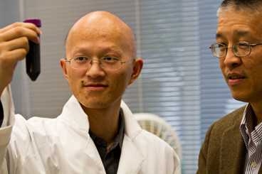 Graduate student Jianjian Wang holds a flask containing the suspension of graphite flakes in hexadecane, as Gang Chen looks on.