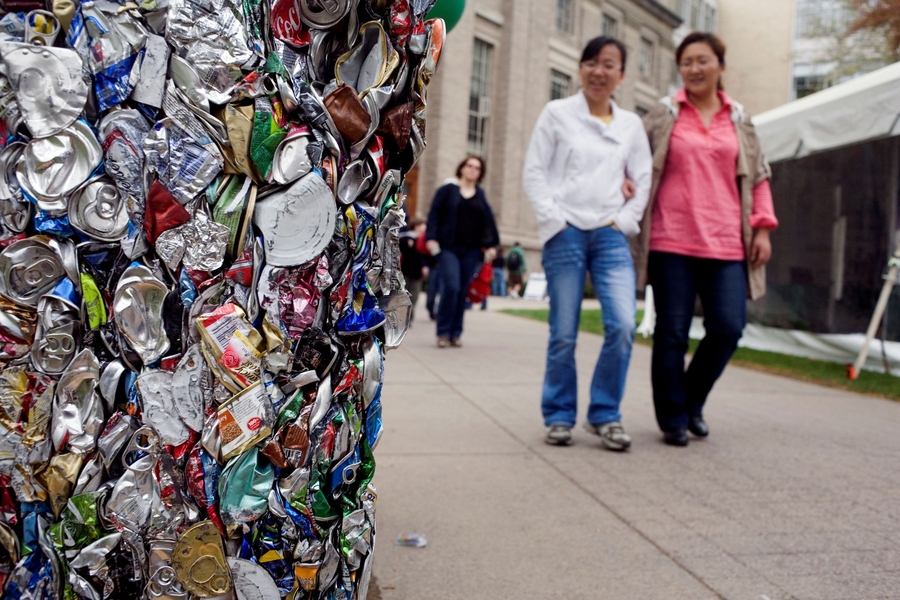 People walk past a block of crushed aluminum cans outside a tent on Eastman Court filled with displays of research focusing on clean energy and sustainable living.