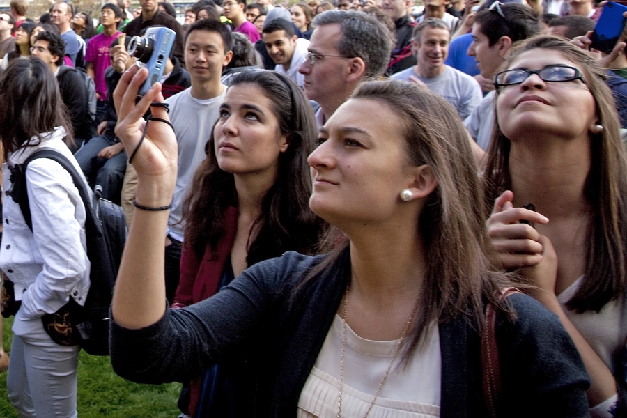 The crowd looks up in anticipation, some with cameras at the ready, moments before the piano is dropped.