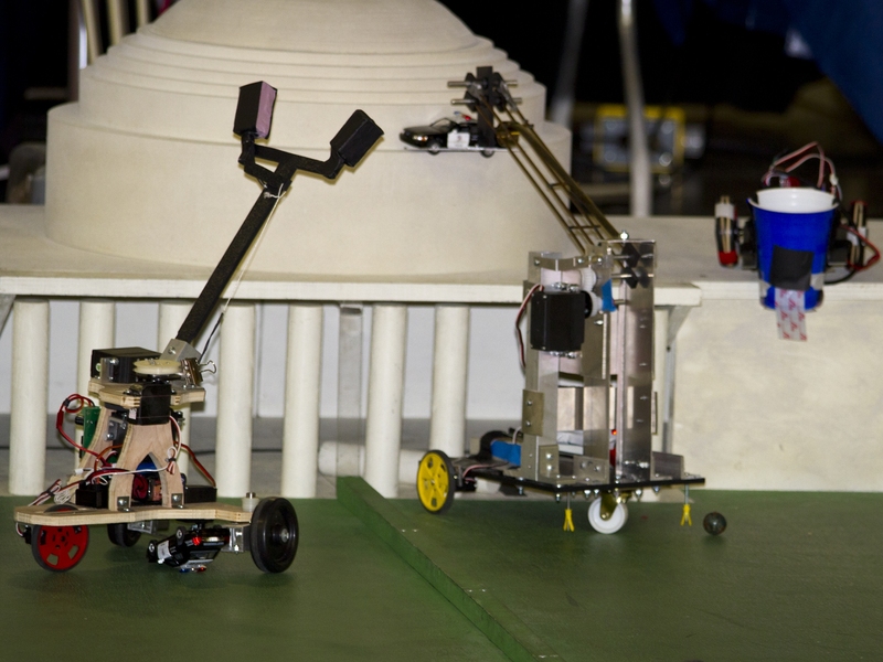 Two robots go head-to-head in an attempt to lift a toy police car onto a scaled-down roof of MIT's iconic dome.