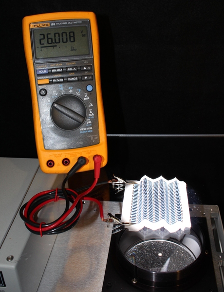 A paper solar cell that has been repeatedly folded is illuminated from below and connected to a voltmeter to demonstrate its output (26 V).