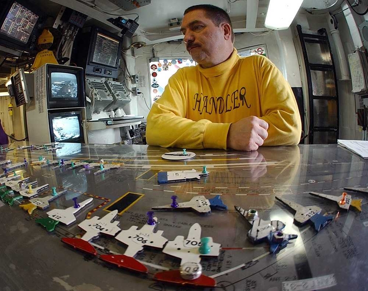 Deck handlers manage traffic on an aircraft carrier by reshuffling tiny model planes on a tabletop model of the flight deck, known as the 'Ouija Board.'