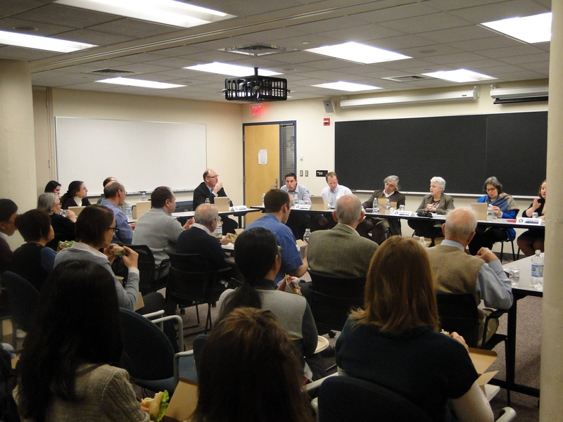 Photo of a classroom with a panel seated at front and many audience members in chairs