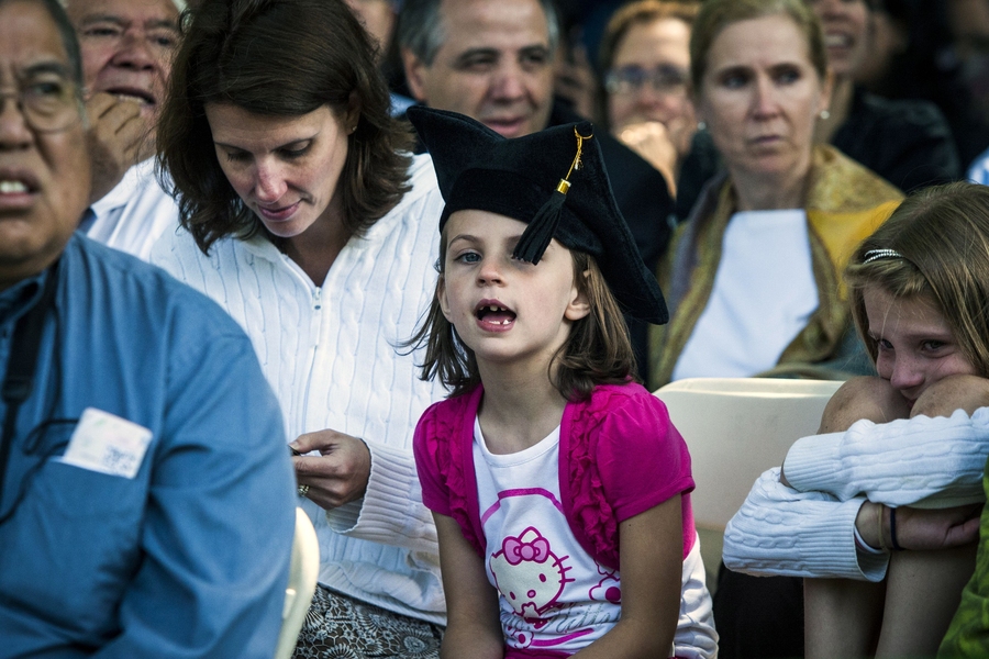 An audience member wears a graduating student's cap.