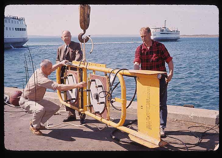 Edgerton (center), Bill MacRoberts (right) and an unidentified man pose by a sonar boomer on a dock at the Woods Hole Oceanographic Institution in 1964.