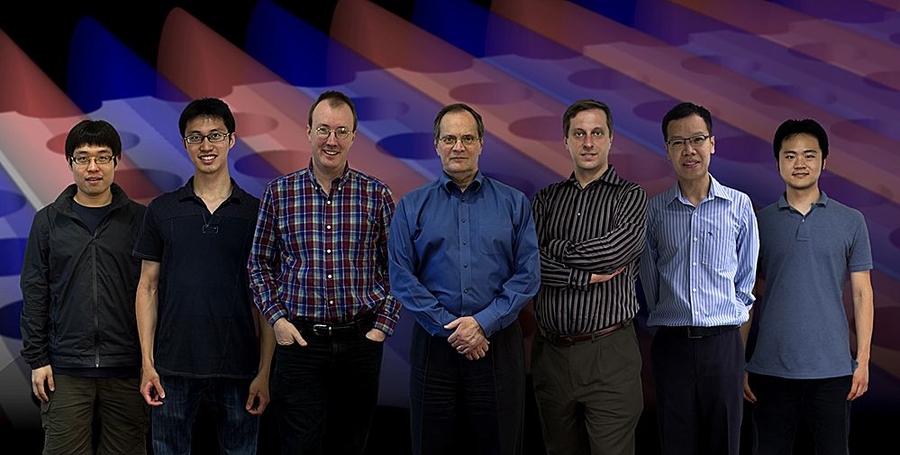 Members of the team that discovered and demonstrated the new way to trap light. From left: Bo Zhen, Chia Wei Hsu, Steven Johnson, John Joannopoulos, Marin Soljačić, Song-Liang Chua and Jeongwon Lee. The background is a snapshot of a theoretical simulation of their system, where light (its electric field shown in blue and red patterns) is confined in a slab with periodic array of holes.