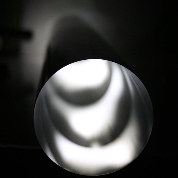 A cylindrical mirror of the type the MIT and NASA researchers have developed for a novel type of neutron microscope is shown on a test stage in the lab, with light reflected through it to test the precision polishing of its shape.

