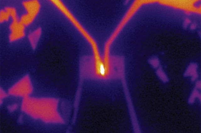 In the team's experimental setup, electricity was supplied to a tiny piece of tungsten selenide (small rectangle at center) through two gold wires (from top left and right), causing it to emit light (bright area at center), demonstrating its potential as an LED material.
