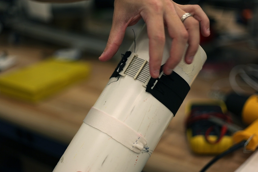 Several actuators aligned into a 3-D-printed cartridge structure, paired with passive fabric to form an active tourniquet, and mounted on a rigid object approximating a human limb.