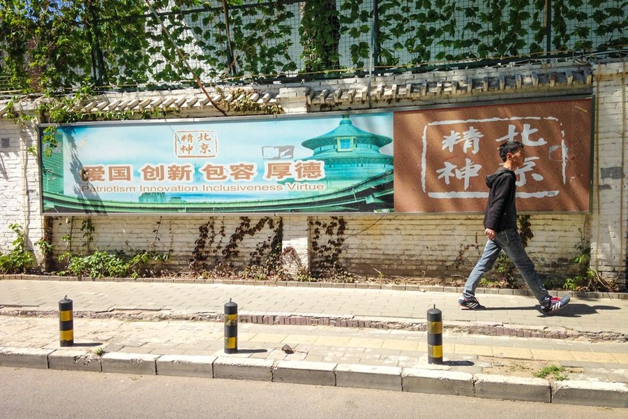 A man walks past a political banner in Guanghua Li that reads, "Patriotism Innovation Inclusiveness Virtue," in Chinese and English.