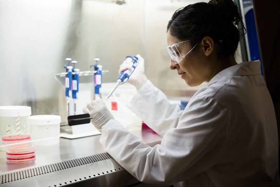 Mariana Matus working in a lab, wearing white lab coat and goggles, pipetting samples