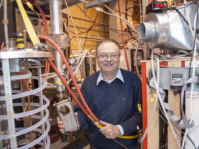 In one hand, senior research engineer Paul Woskov holds orange water cooling lines that lead to the rock test chamber (left foreground), and in the other the result of drilling rock with a gyrotron beam.